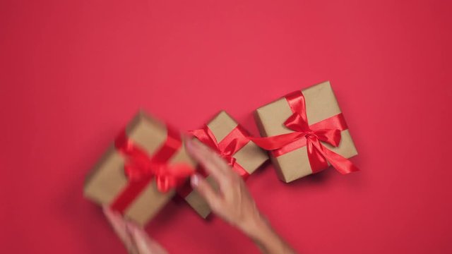 Woman hands placing carelessly group of gift boxes over red flat lay