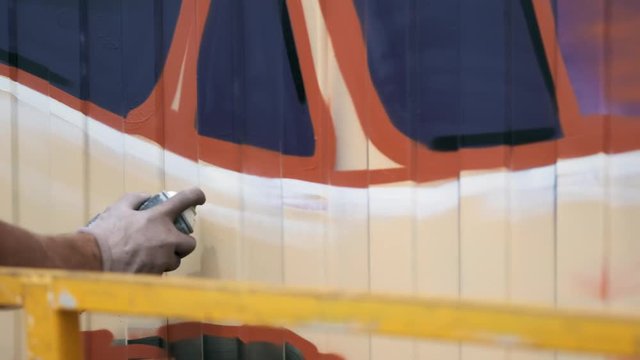 A young guy with a can of paint draws graffiti on the wall. One hand close-up