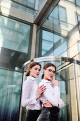Obraz premium two young pretty business women against a modern glass office building
