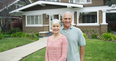 Senior couple standing smiling in front of new home