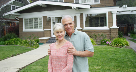 Senior couple standing smiling in front of new home