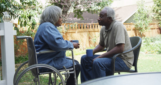 Senior African woman in wheel chair outdoors with husband
