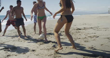 Healthy group of friends running playing soccer on beach