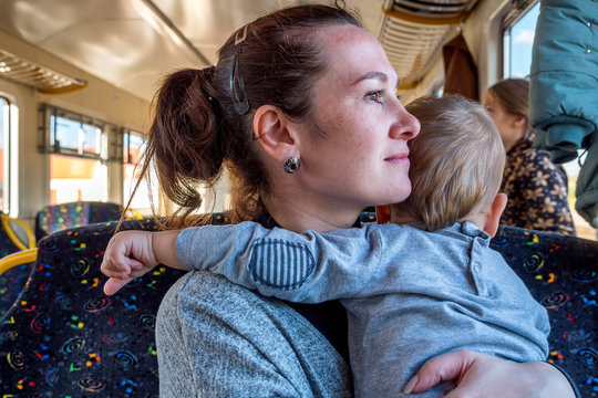 Young Happy Mother Holding Baby While He Pulls Her Hair While Travelling By Train