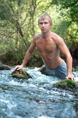 young man stands in a sports rack on the rocks of a mountain river