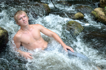 handsome man resting on the river lying in a waterfall among the stones