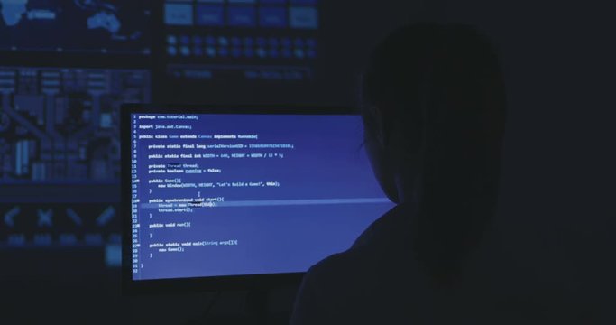 Experienced IT woman programmer works on a new program. Young woman hacker writes the source code of the software at dark room. Back view.