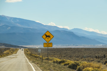 A heat shimmer on the road and cars in the high desert with mountains in the distance and a sign with a horse that says Open Range