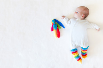 A baby one month is lying on a white background. White clothes. A bright colored toy hare rabbit.