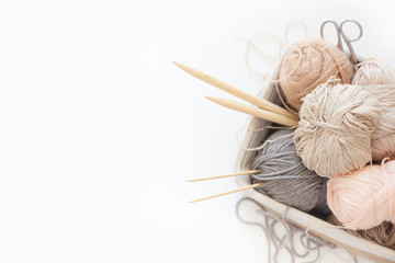 Neutral beige yarn for knitting is in the basket. Knitting needles, scissors. White background.