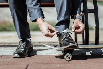 Tuinposter Perfect style. Close up of tender male hands binding laces and preparing for riding on skateboard © zinkevych
