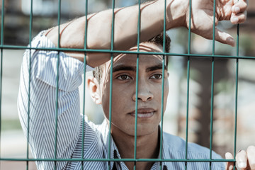 Future success. Tranquil serious guy gazing aside while touching fence