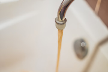 Dirty brown running water falling into a white sink from tap. Environmental pollution concept
