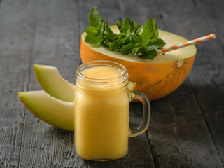 Half a melon with mint and a cocktail straw and a mug of smoothies on a wooden table.