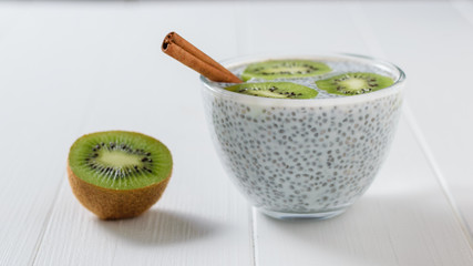 Cinnamon sticks, kiwi fruit and a glass bowl of Chia seeds with milk on the white table.