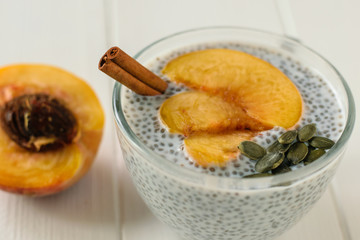 Chia seed pudding with peach and pumpkin seed on a white wooden table.