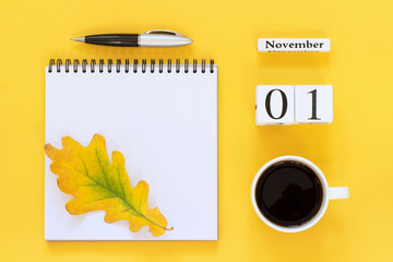 Autumn composition. Wooden calendar November 1 cup of coffee, empty open notepad with pen and yellow oak leaf on yellow background. Top view Flat lay Mockup Concept Hello November