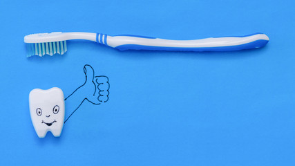 A fun tooth figurine puts a toothbrush class on a blue background. The view from the top. Flat lay.
