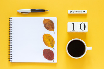 Autumn composition. Wooden calendar November 10 cup of coffee, empty open notepad with pen and yellow oak leaf on yellow background. Top view Flat lay Mockup Concept Hello November