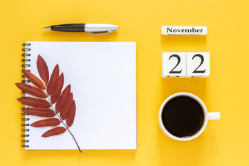 Autumn composition. Wooden calendar November 22 cup of coffee, empty open notepad with pen and yellow oak leaf on yellow background. Top view Flat lay Mockup Concept Hello November