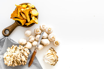 Fototapeta na wymiar Cook mushrooms concept. Champignons, oysters, chanterelles on frying pan and near knife on white background top view copy space