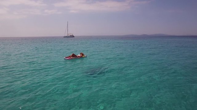 Aerial - Woman relaxing on inflatable mattress in crystal clear water near ancho