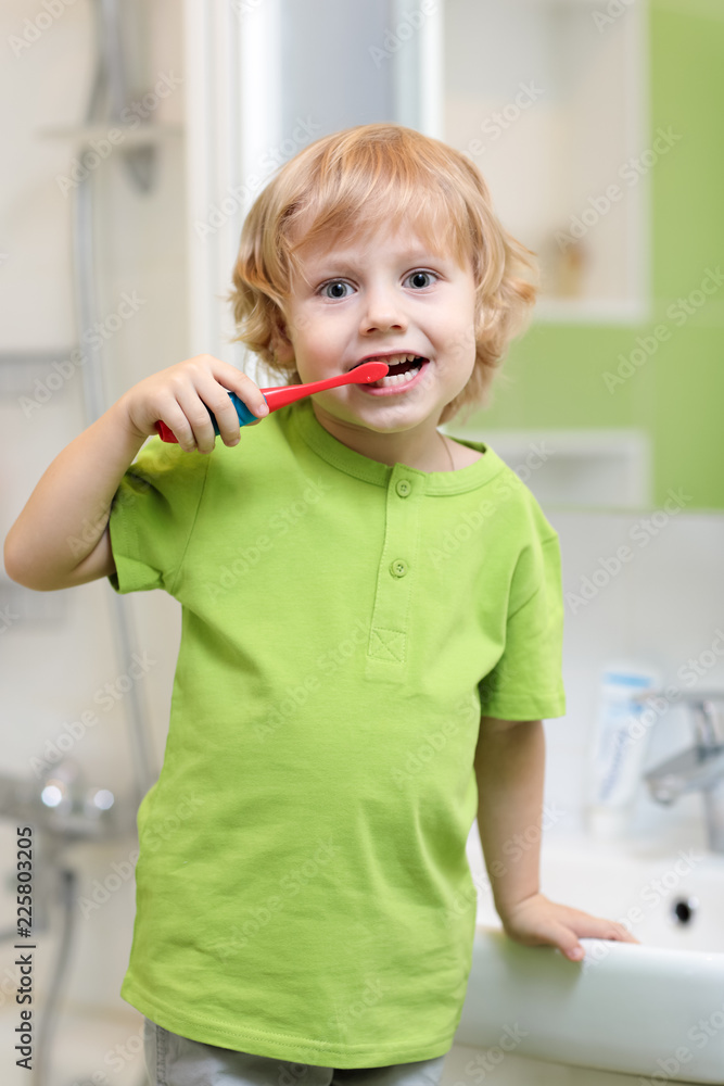 Wall mural Cute little child boy brushing his teeth in bathroom