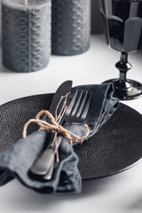 Festive table setting in a black style among black candles. Plate with fork and knife on a linen...