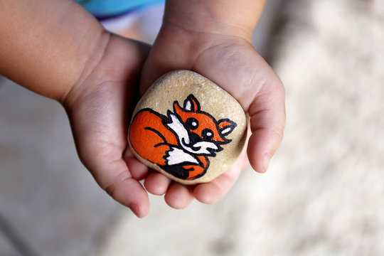 Young Child's Hands Holding a Painted Rock with A Cartoon Fox on It