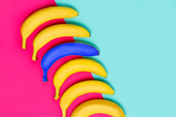 Bright blue banana among yellow fruits on pink and pastel blue background,
