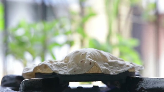 footage of making of Phulka a kind of Chapati: Indian thin bread made from wheat dough being baked on gas stove in home.