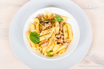 Pasta with bacon and cheese sauce in a plate on a light wooden table