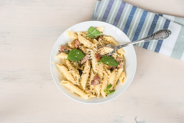 Traditional dish of Italian cuisine - penne pasta with pancetta, parmesan cheese and basil on a plate close-up, top view