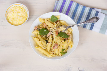 Traditional dish of Italian cuisine - penne pasta with pancetta, parmesan cheese and basil on a plate close-up, top view