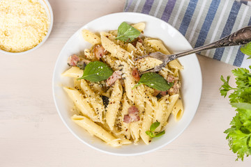 Traditional dish of Italian cuisine - penne pasta with pancetta, parmesan cheese and basil on a plate close-up, top view