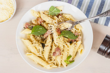 Traditional dish of Italian cuisine - penne pasta with pancetta, parmesan cheese and basil on a...