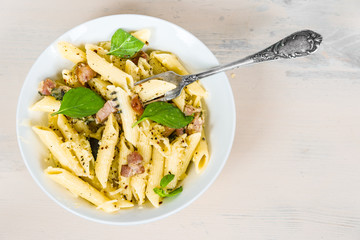 Mediterranean cuisine - penne pasta with pancetta, parmesan cheese and basil on a plate close-up, top view, copy space