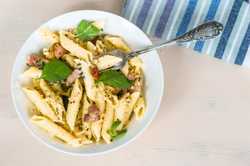 Mediterranean cuisine - penne pasta with pancetta, parmesan cheese and basil on a plate close-up, top view, copy space
