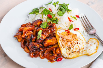 Thai food - chicken in spicy sauce with rice and fried egg close-up.