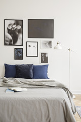 White industrial style floor lamp by a cozy bed with dark blue cushions in a bright hipster bedroom interior