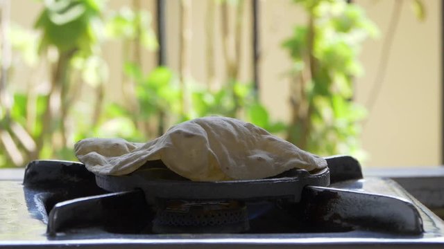 footage of making of Phulka a kind of Chapati: Indian thin bread made from wheat dough being baked on gas stove in home.