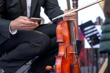 The violinist holds a violin and a mobile phone during a break between performances at the concert_ © Volodymyr