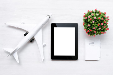 Toy airplane and mobile tablet computer with blank screen on white wooden table background.