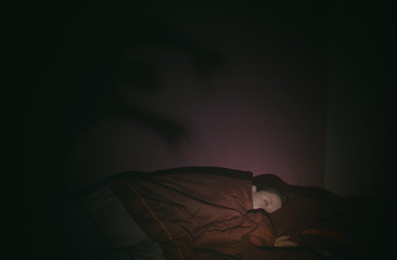 Sleeping girl in the bed and shadow of monster on the wall behind. Nightmare concept.