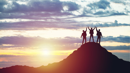 Silhouettes of happy three people on top of a mountain