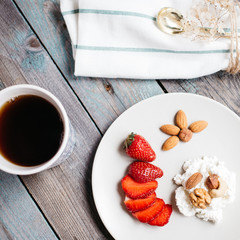 a plate with cottage cheese, strawberries and nuts, a cup of coffee and towels on a wooden table, healthy food, breakfast