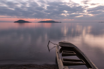 Beautiful view of Trasimeno lake (Umbria) at dusk, with a little, old boat partially filled by water, perfectly still water and a mackerel sky