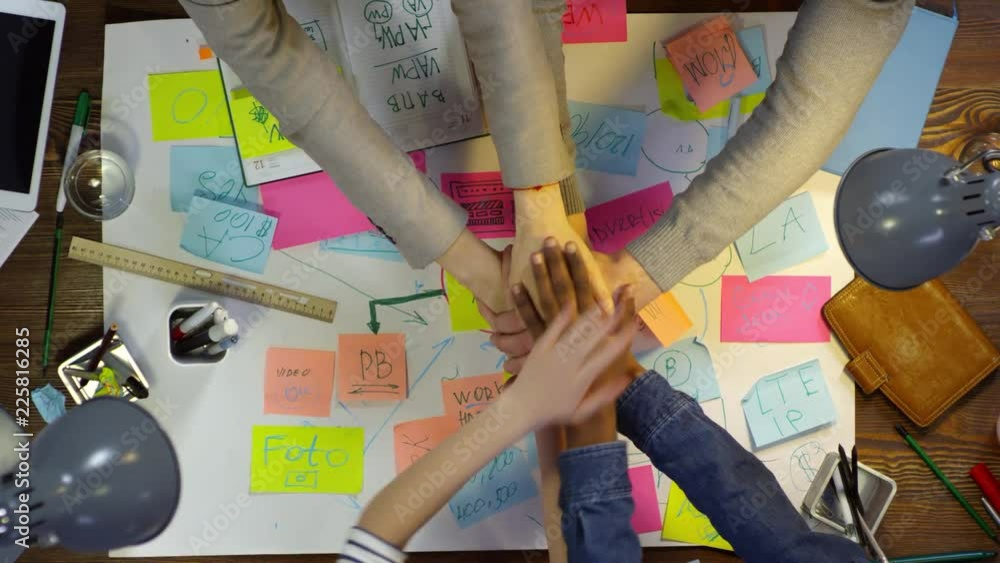 Poster top view of hands of unrecognizable business people making stack of hands while sitting at desk with