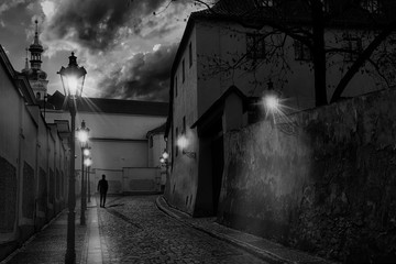 Mysterious narrow street of Prague at sunset with the silhouette of a man walking and all the street lights on creating shadows