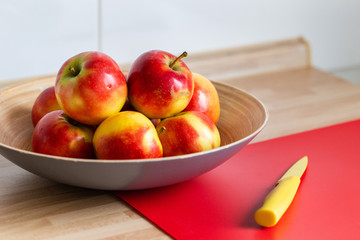 rot gelbe &auml;pfel in einer obstschale,mit einem roten schneidebrett und einem gelben messer 